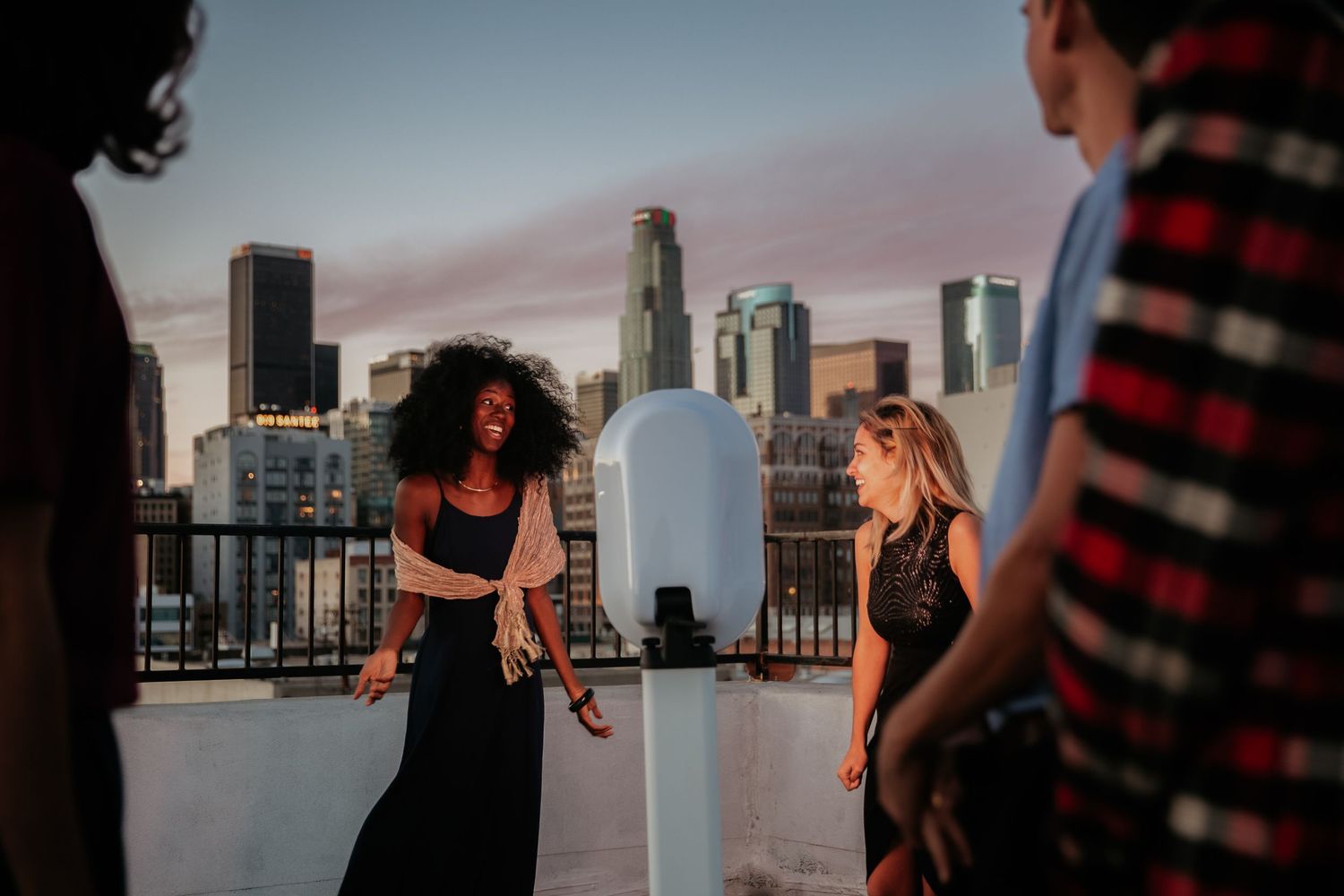 Friends enjoying a rooftop gathering at sunset with Los Angeles downtown skyline in the background.