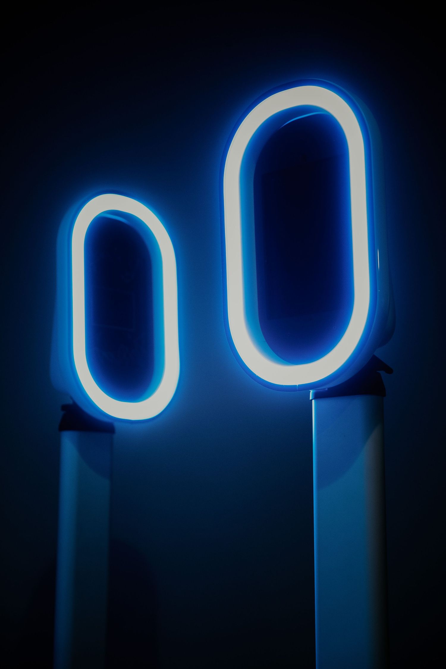 Two illuminated blue neon oval shapes mounted on white stands against a dark background.