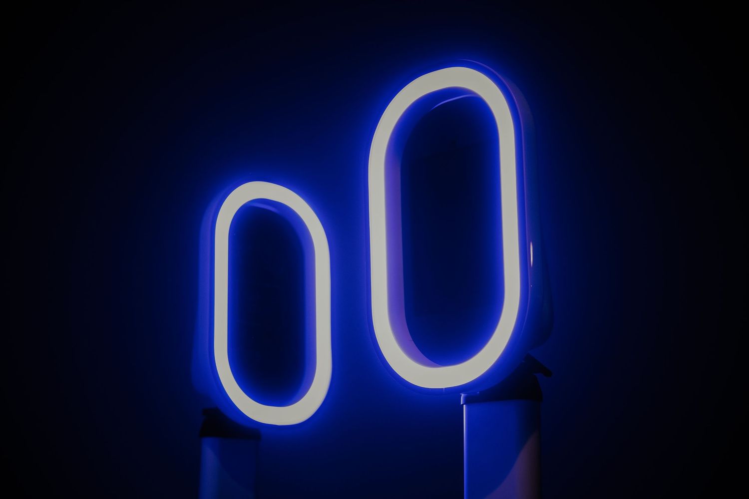 Two oval-shaped illuminated frames glowing in blue neon light against black background.