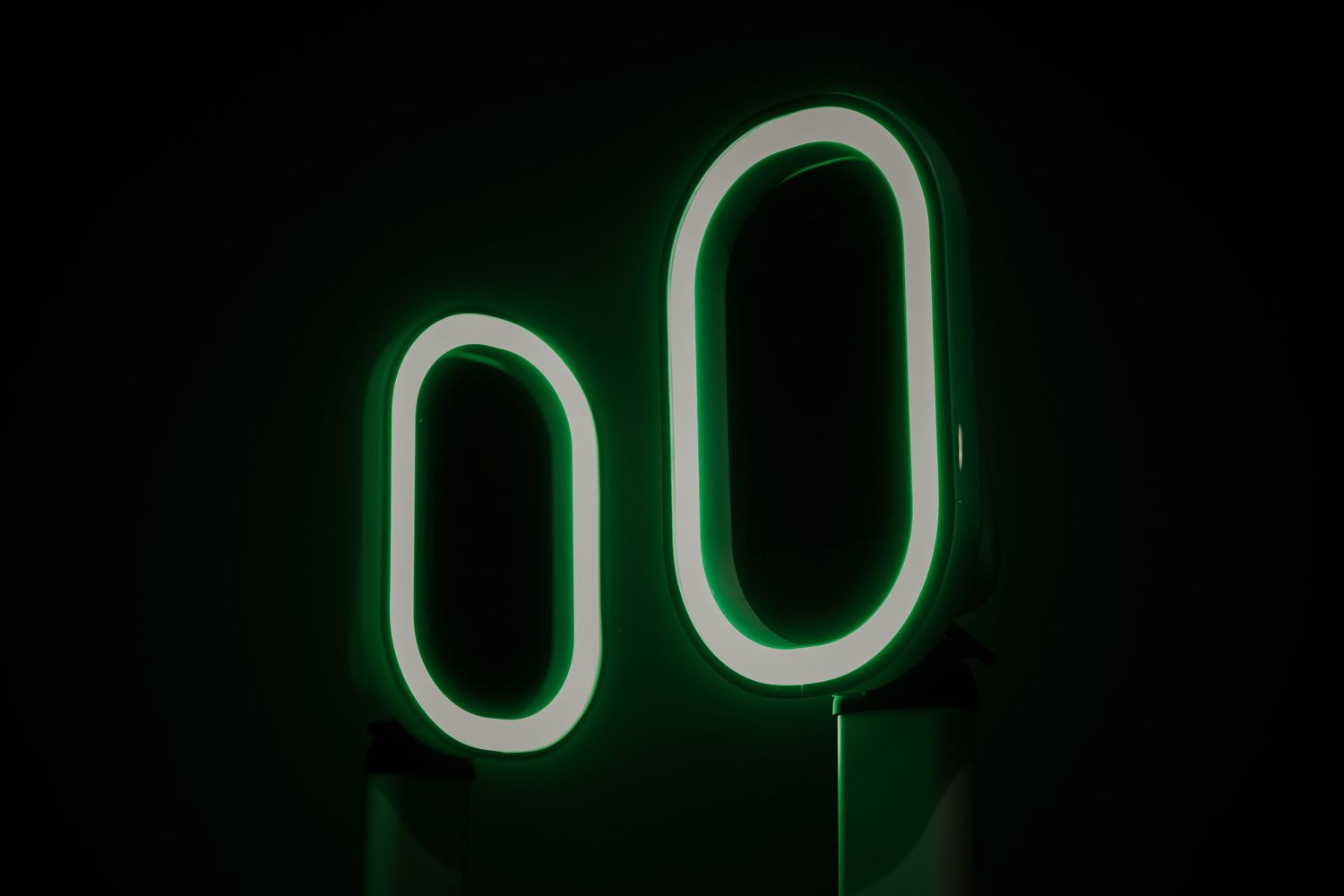 Two green neon oval shapes glowing against a black background creating a minimalist geometric design.