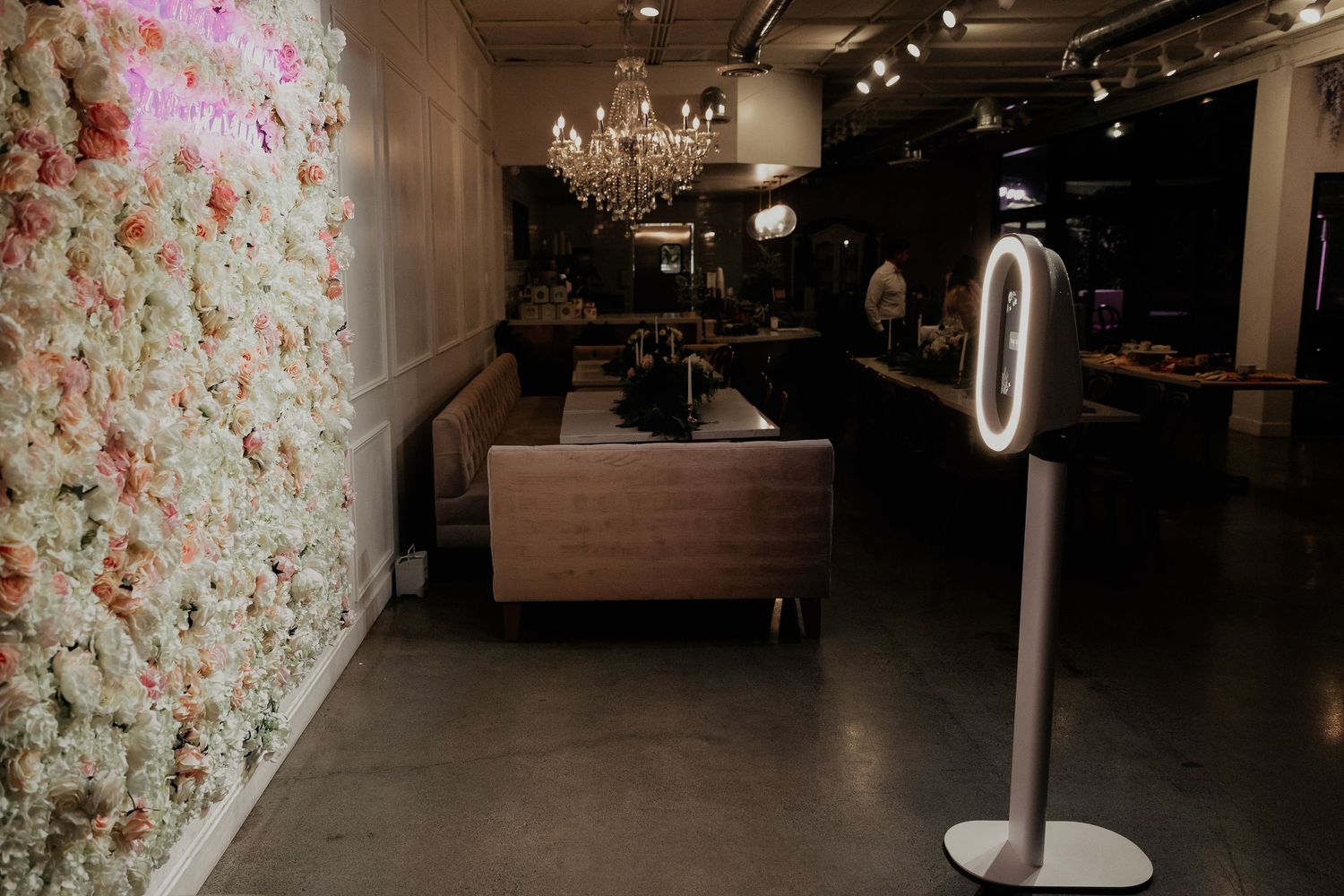 Modern salon interior with floral wallpaper, chandelier lighting, and ring light stand in a moody dark setting.