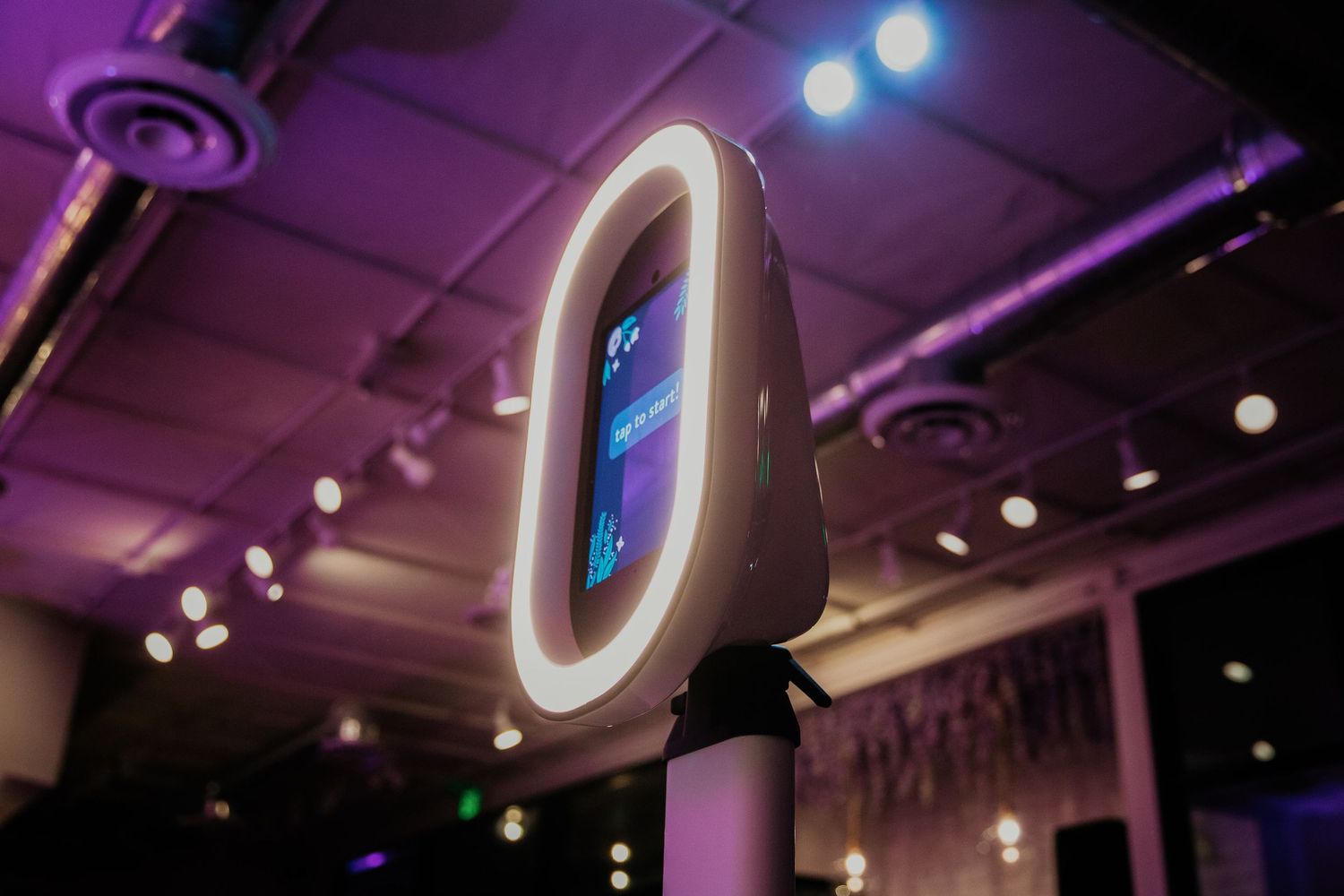 Illuminated neon number zero glows in purple and blue against dark warehouse ceiling with spotlight fixtures.