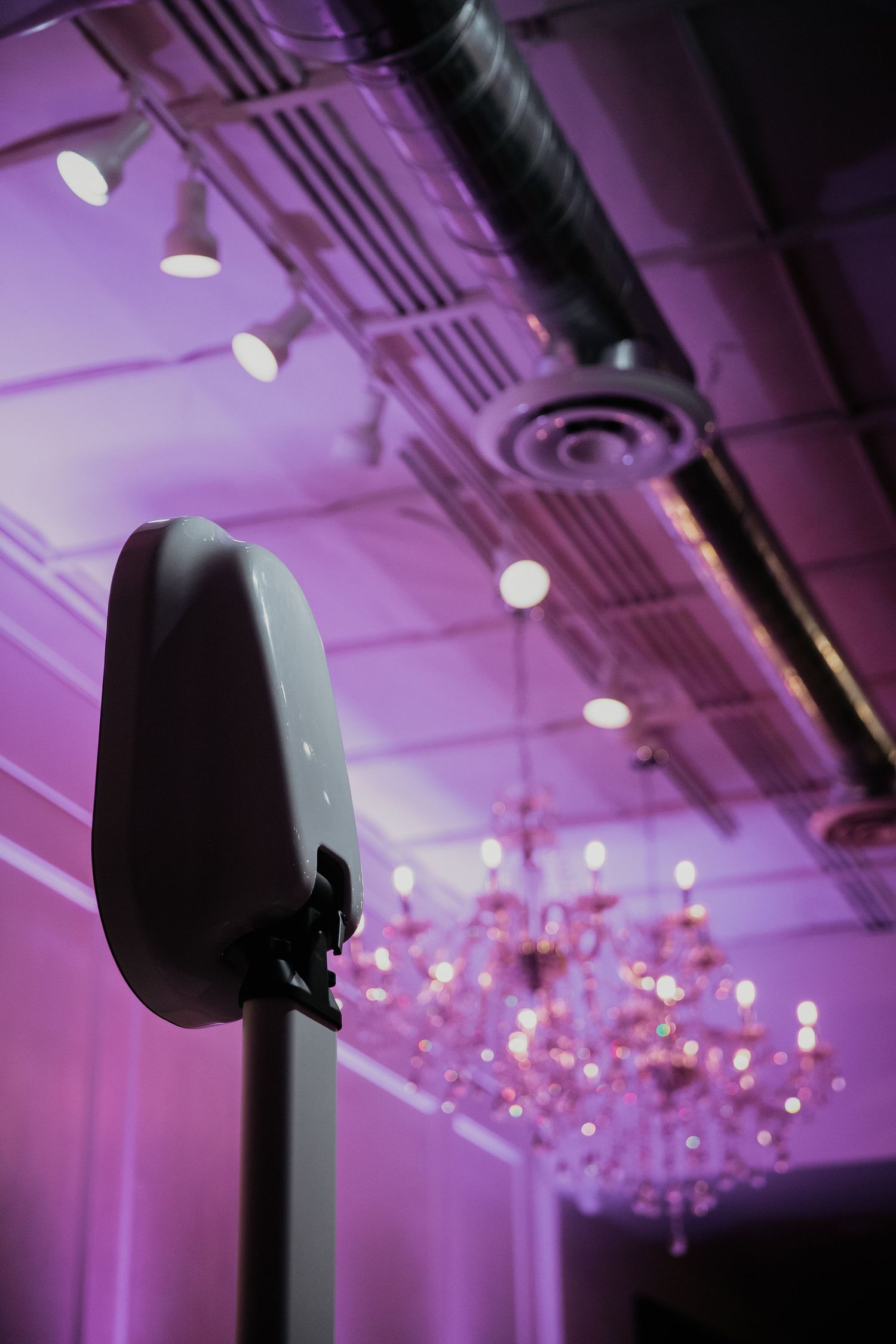 A microphone silhouette against a purple-lit ceiling with a crystal chandelier in the background.