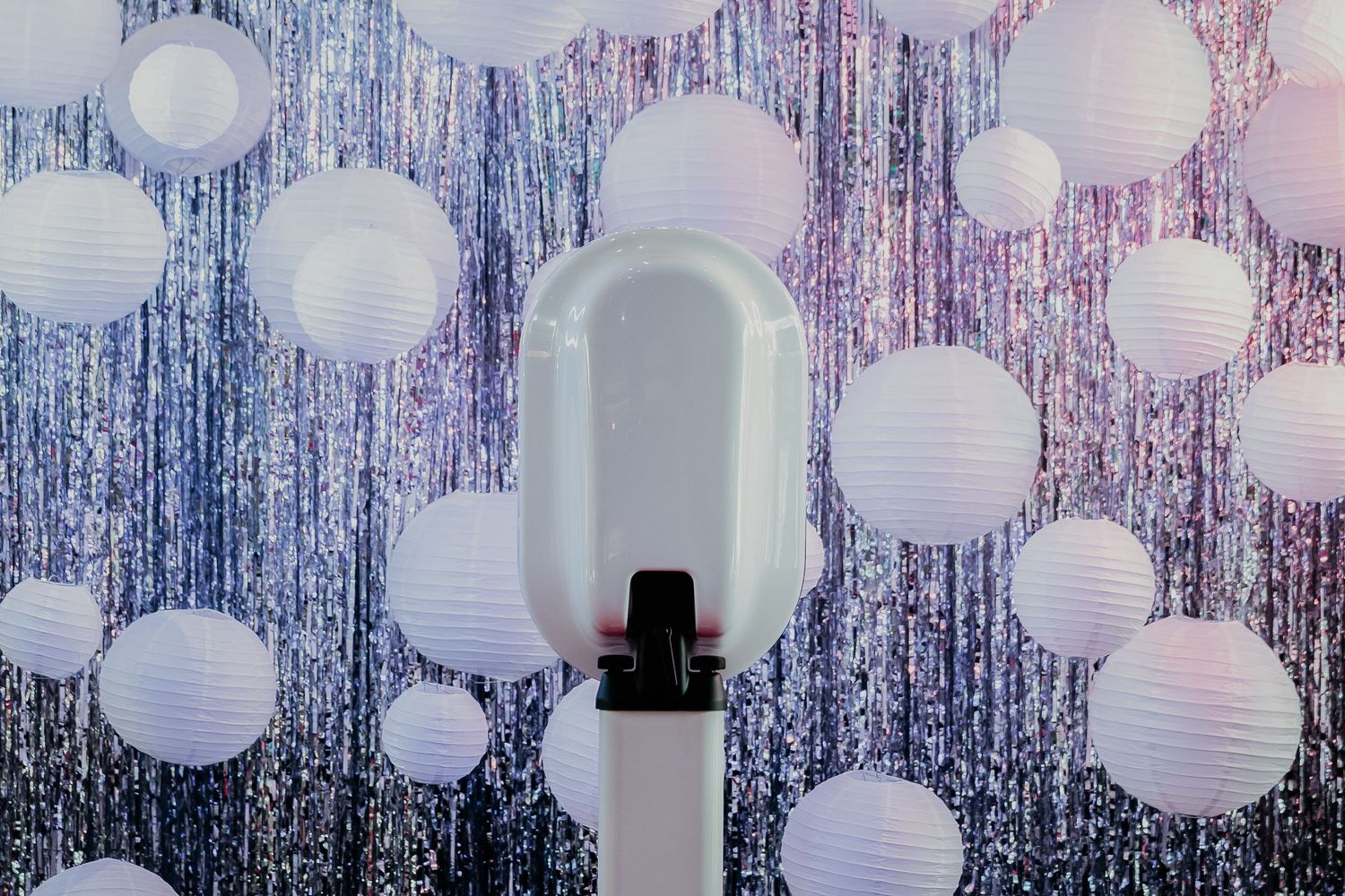 White paper lanterns hang against a sparkly silver tinsel backdrop creating an ethereal party decoration display.