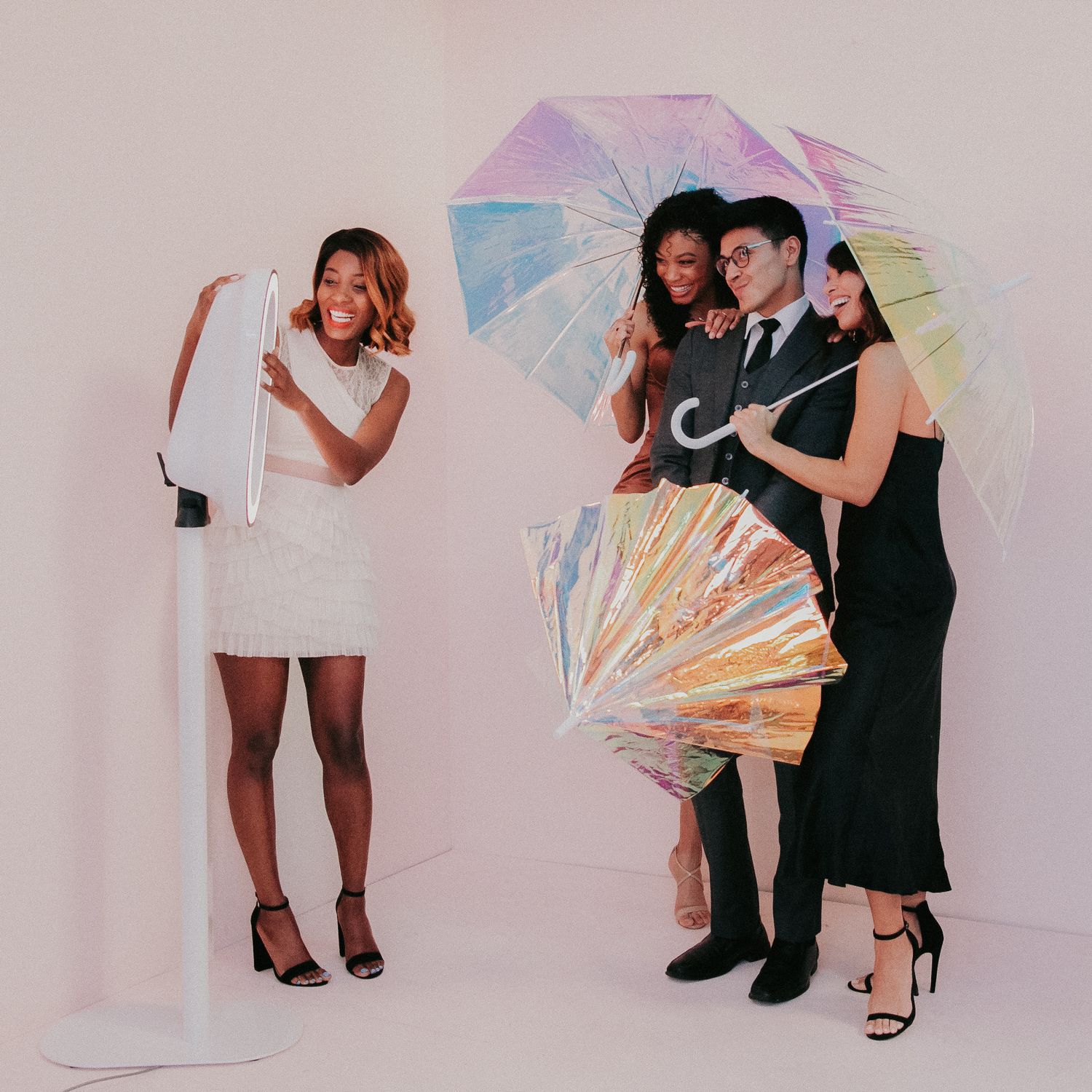Group of fashionable party guests posing with iridescent umbrellas against pink wall during a photo shoot.