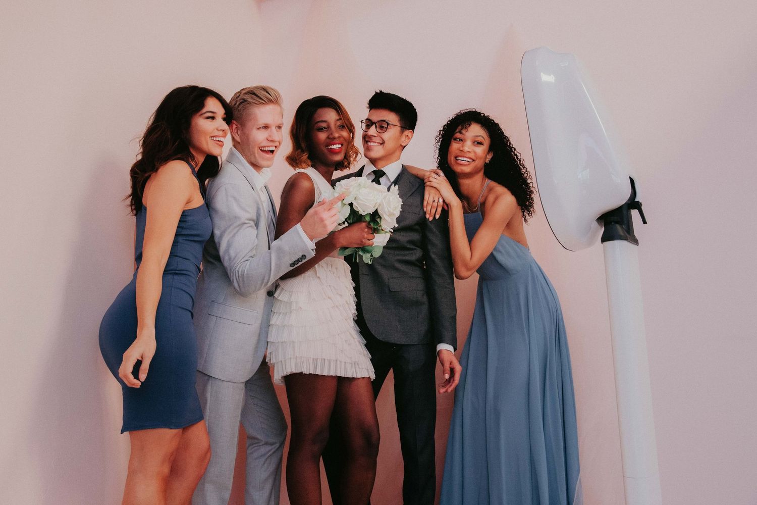 A group in formal attire poses together at a wedding celebration with blue and light-colored dresses and suits.