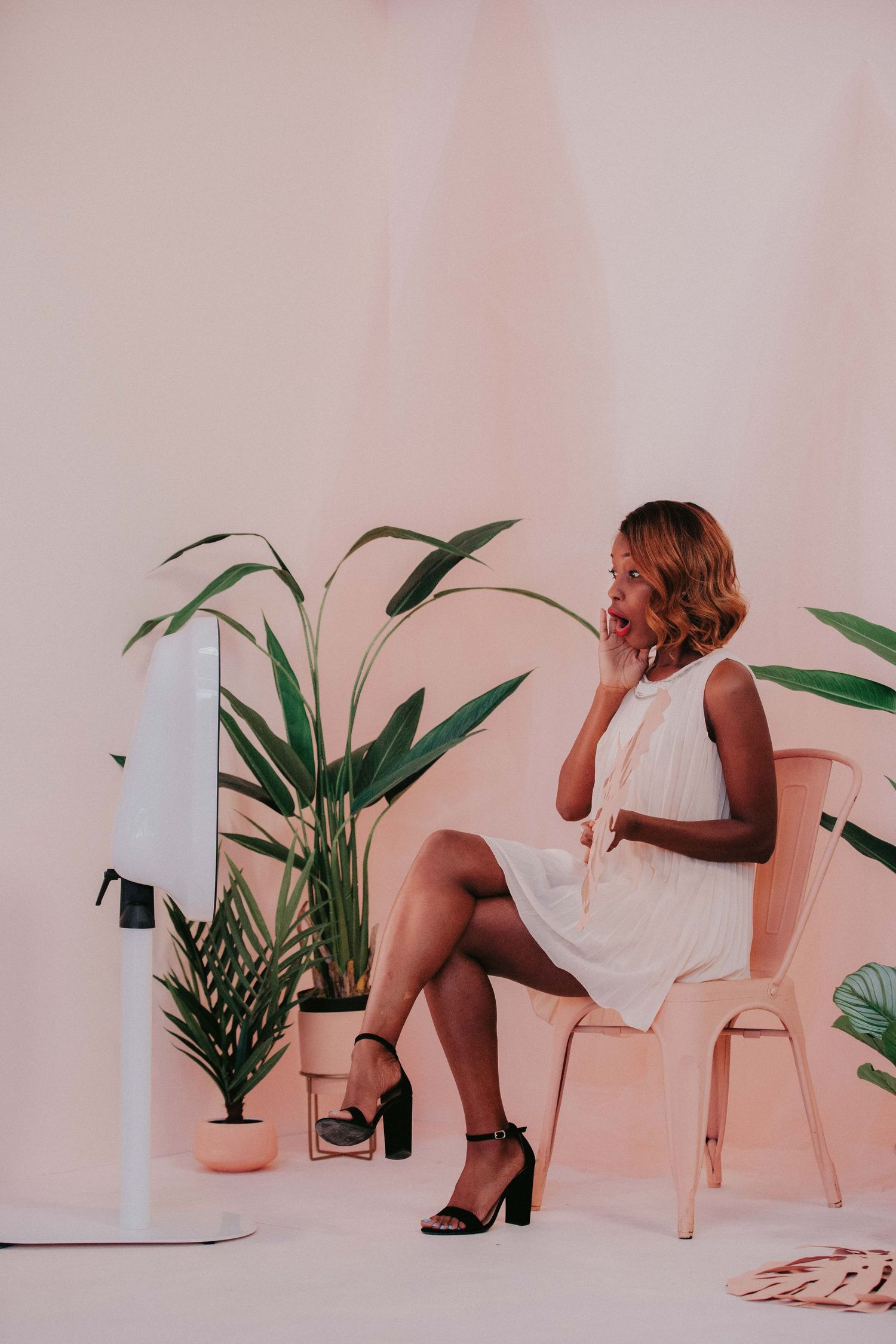 A collage of four similar feminine poses on pink chairs against a soft pink wall with potted plants as decoration.