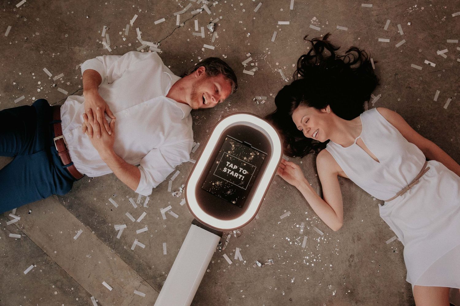 Two people in white outfits lying on concrete floor next to an electronic device displaying text.