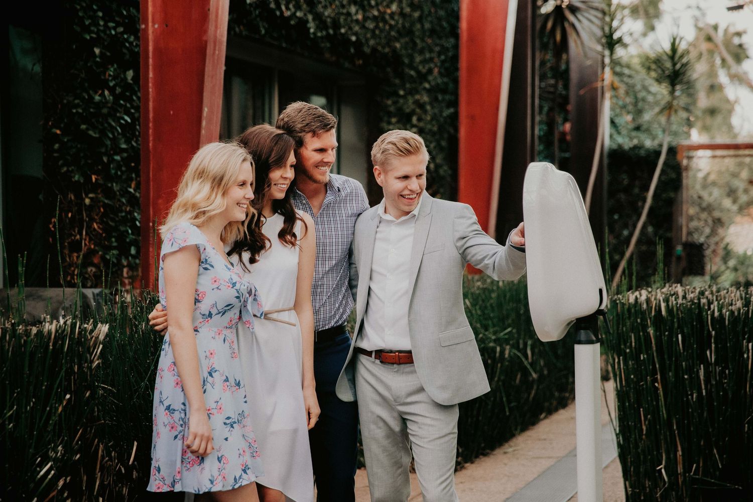 A group of people in formal attire walking together outdoors along a path with red pillars and green foliage.