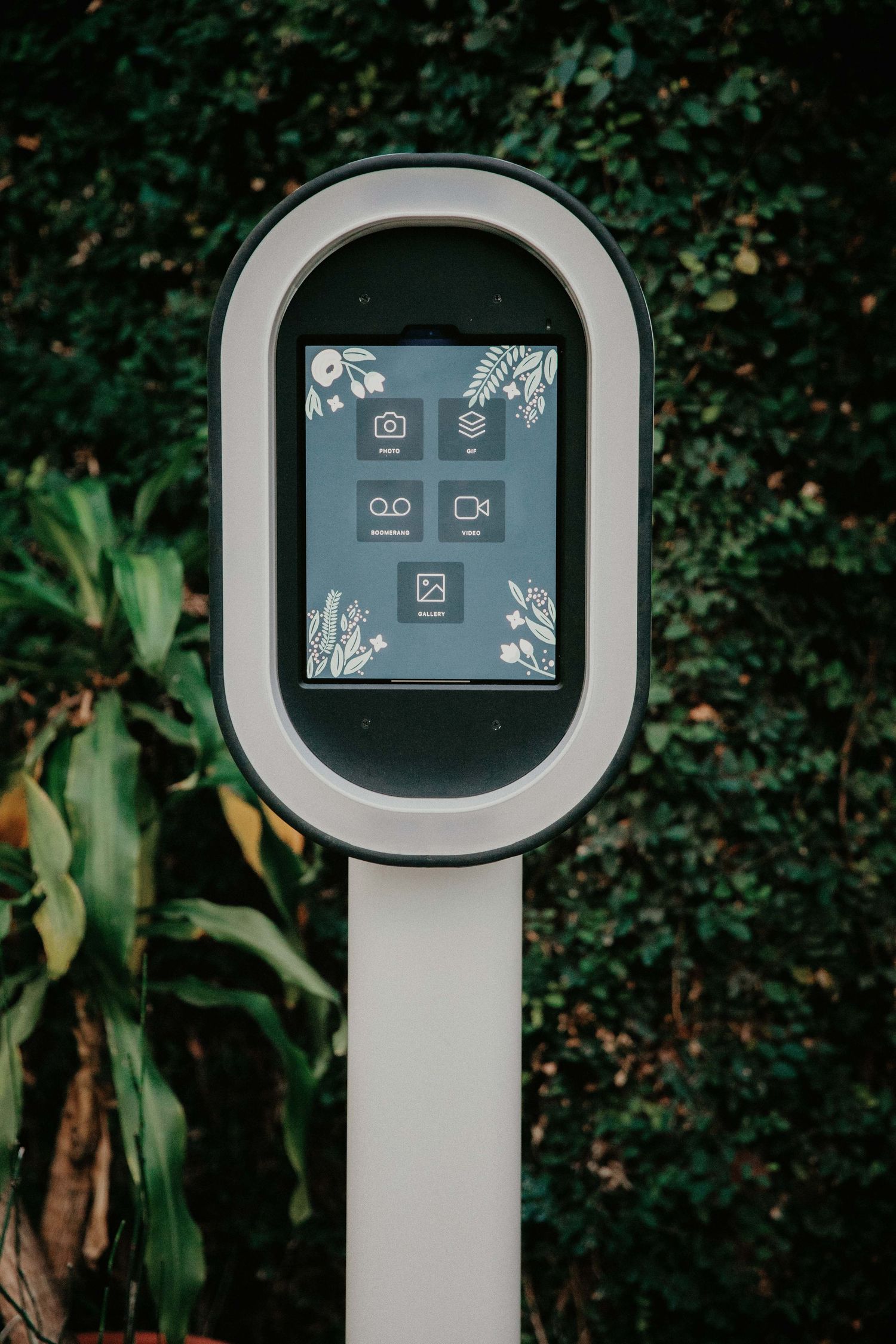 A sleek digital interface kiosk displays menu icons against a green garden background.