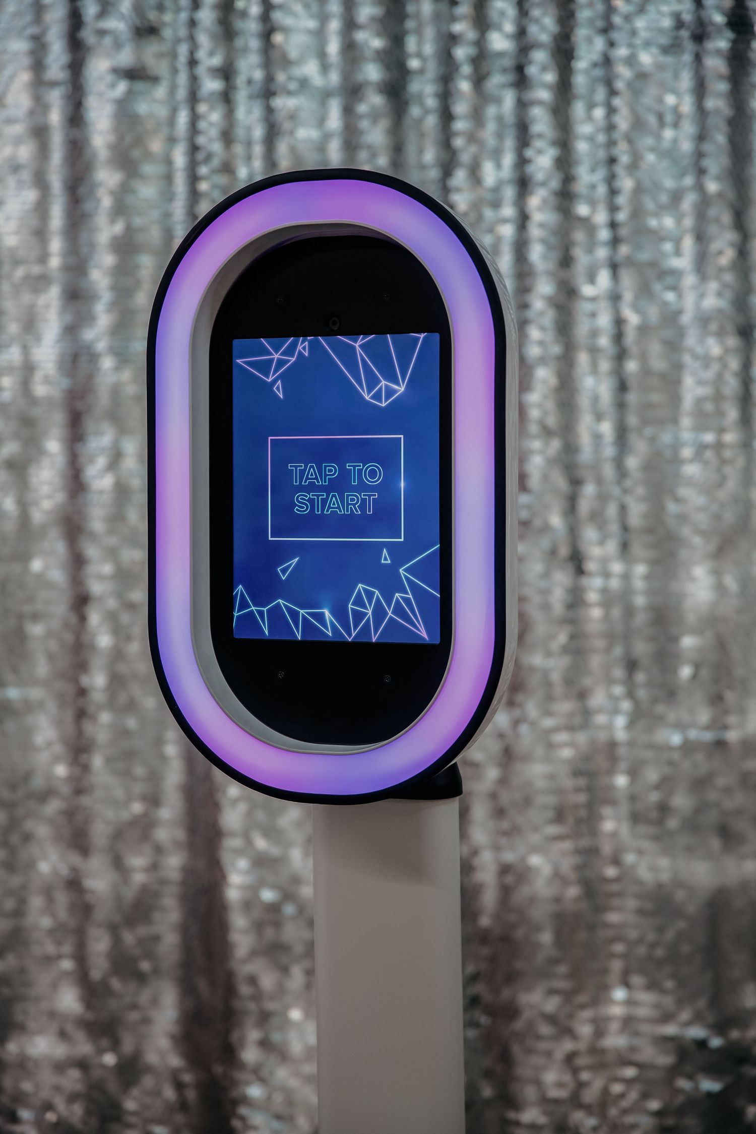 An oval-shaped digital display with a purple frame showing a blue 'Tap to Start' screen against a textured background.