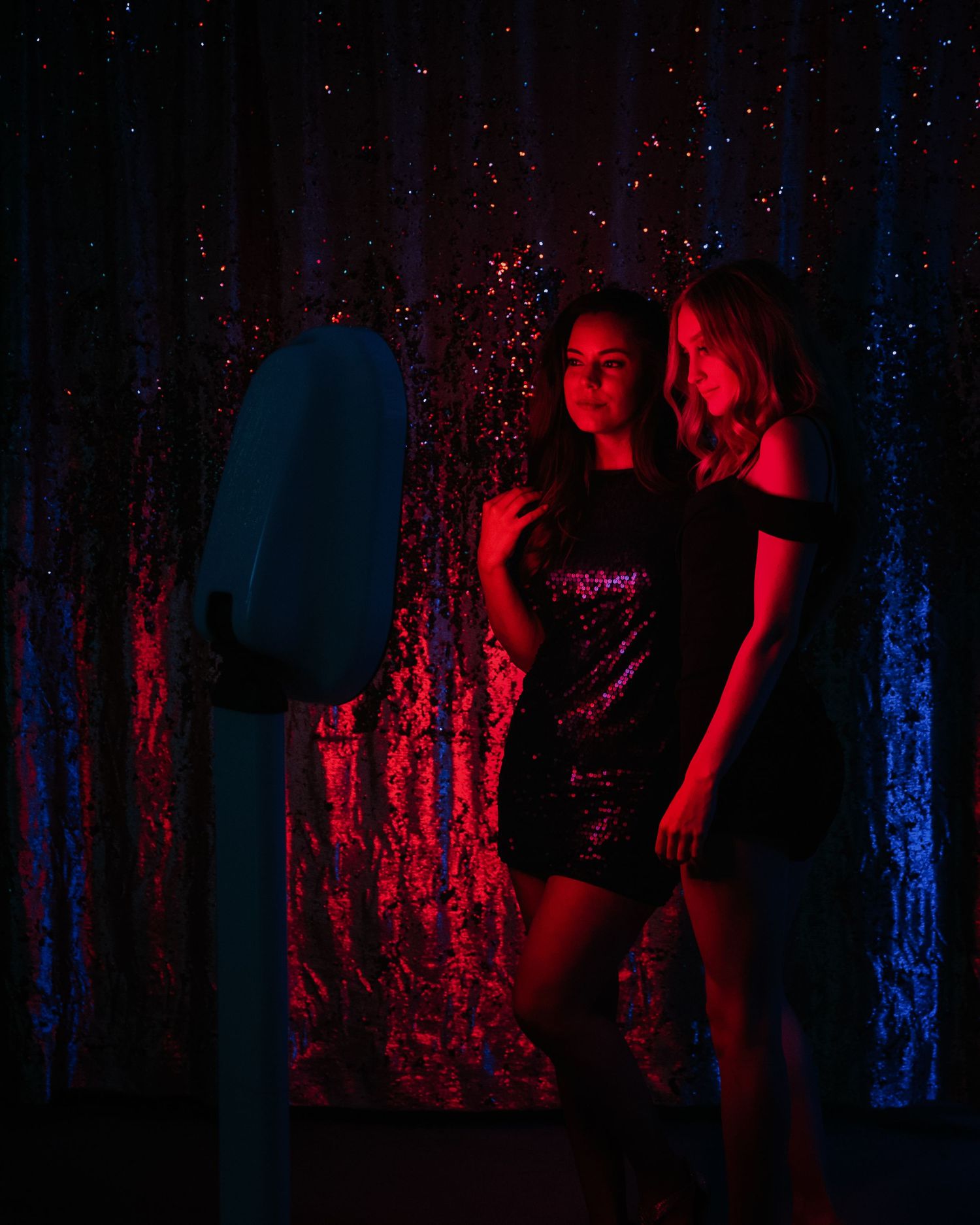 Artistic portrait in moody lighting with dramatic red and blue illumination against a textured backdrop.