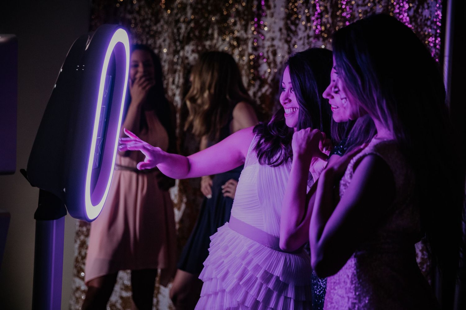 People gather around a glowing purple LED photo booth stand at a nighttime event.