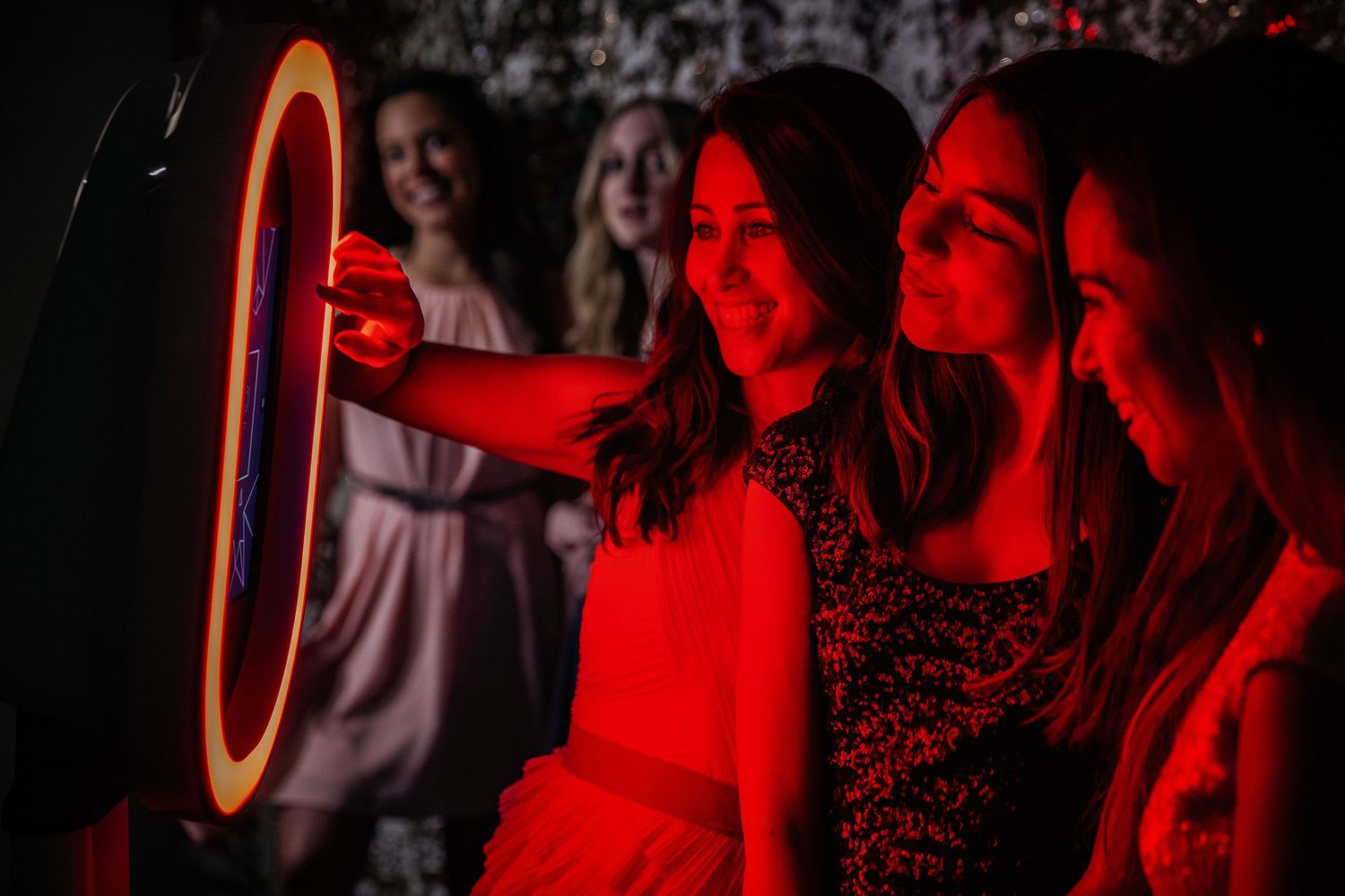 People bathed in red light stand near an illuminated ring light creating a moody atmospheric scene.