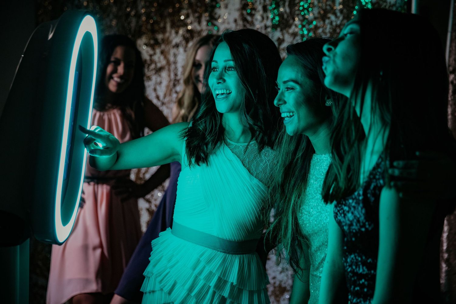 People enjoy taking pictures with a glowing neon ring light casting vibrant turquoise illumination in a dark space.