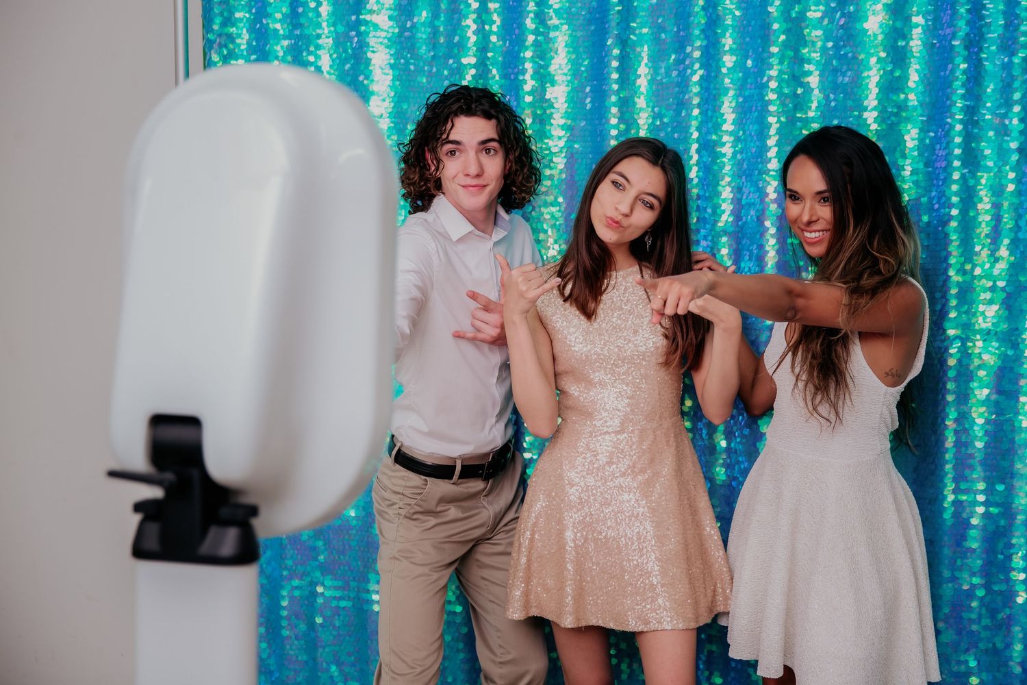 Three friends having fun posing together in front of a sparkly turquoise backdrop at a photo booth.