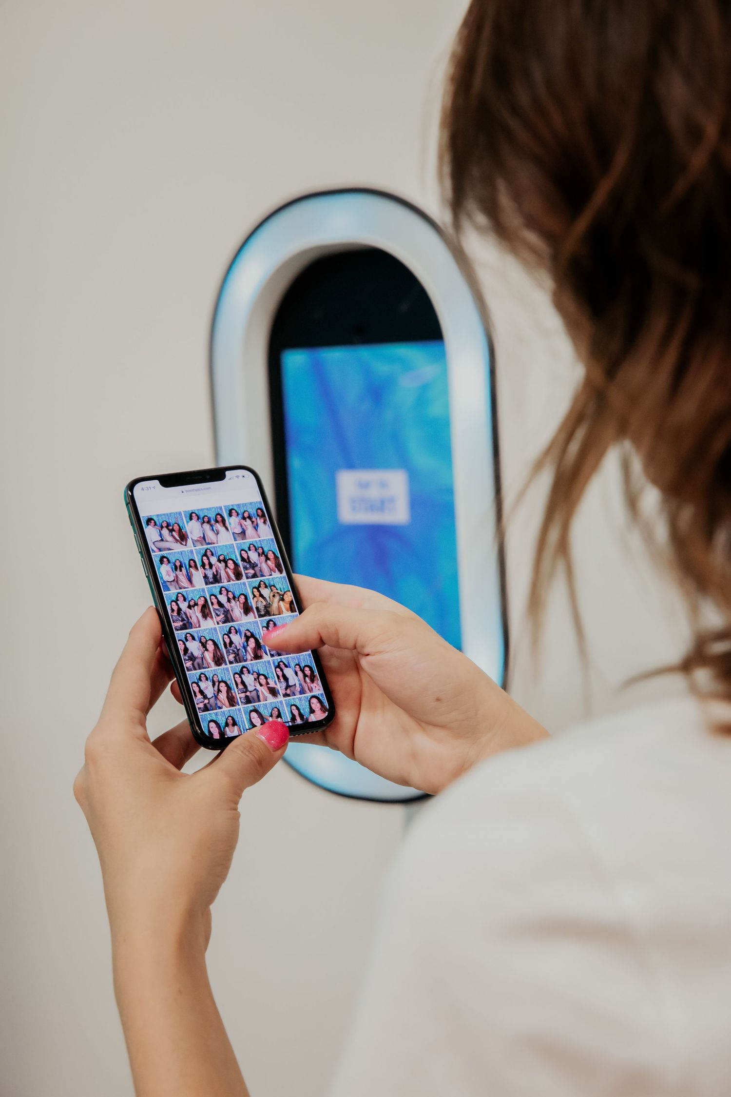 Person looking at smartphone while standing in front of digital device with glowing blue screen on wall.