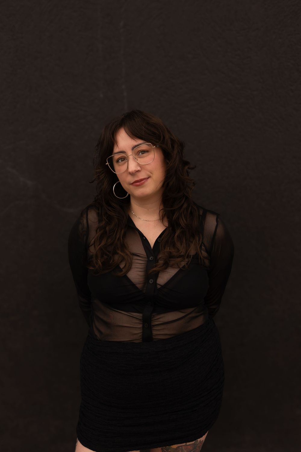 A woman in a black outfit poses against a dark background in a series of moody portrait shots.