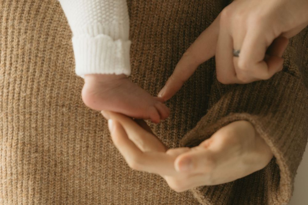 Two hands gently touching while wearing cozy knit sweaters in warm neutral tones.