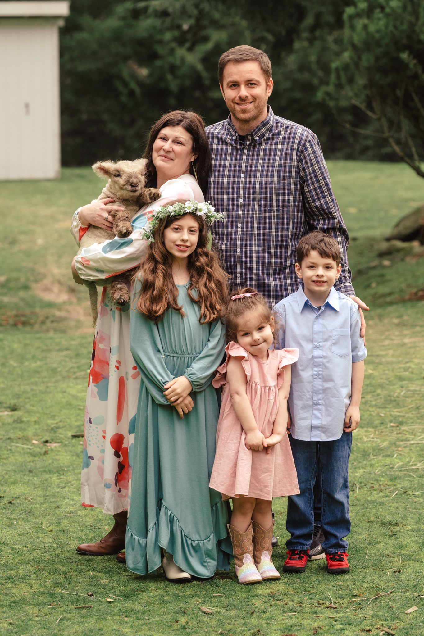 A family of five poses outdoors with their small dog, wearing coordinated spring outfits on a grassy lawn.