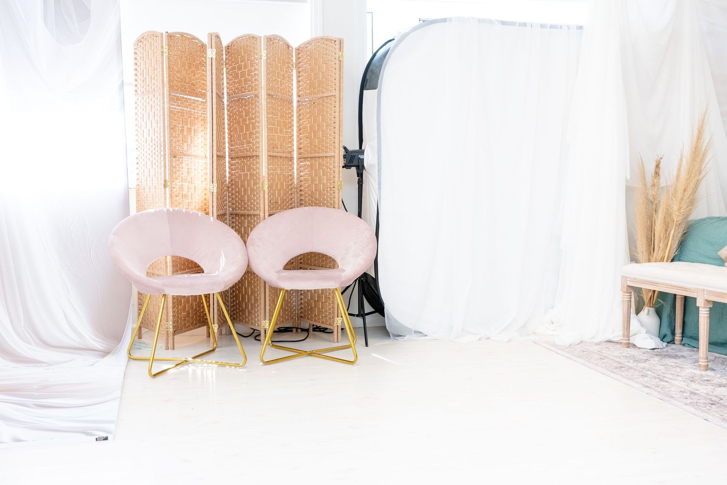 Modern photography studio with pink chairs and bamboo divider screens against white walls and natural lighting.