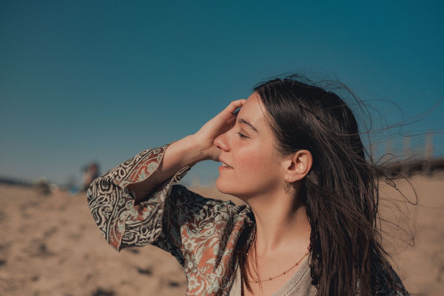 A person with windswept hair poses against a desert background under a blue sky.