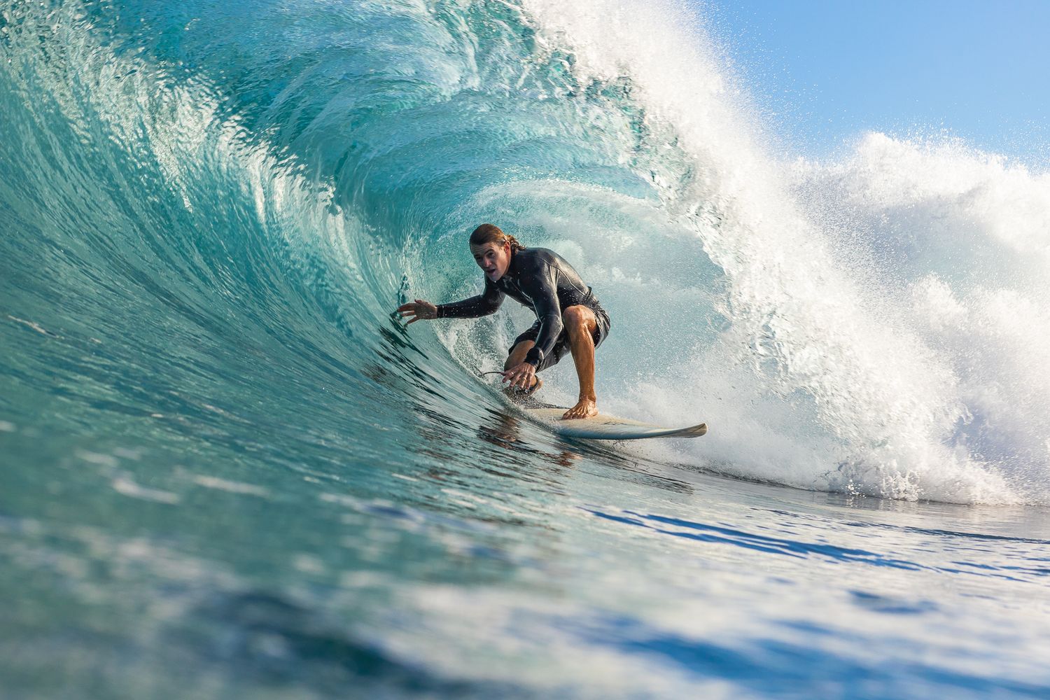 A surfer rides the curl of a beautiful turquoise ocean wave on a sunny day.