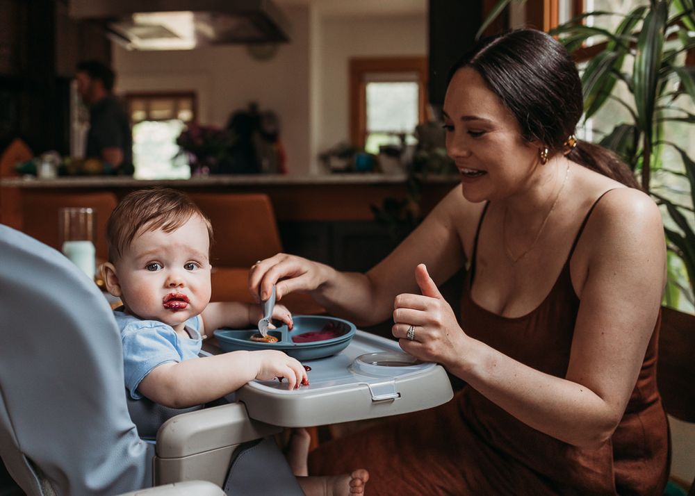Parent and baby seated at dining table with toddler positioned in a blue highchair during mealtime.
