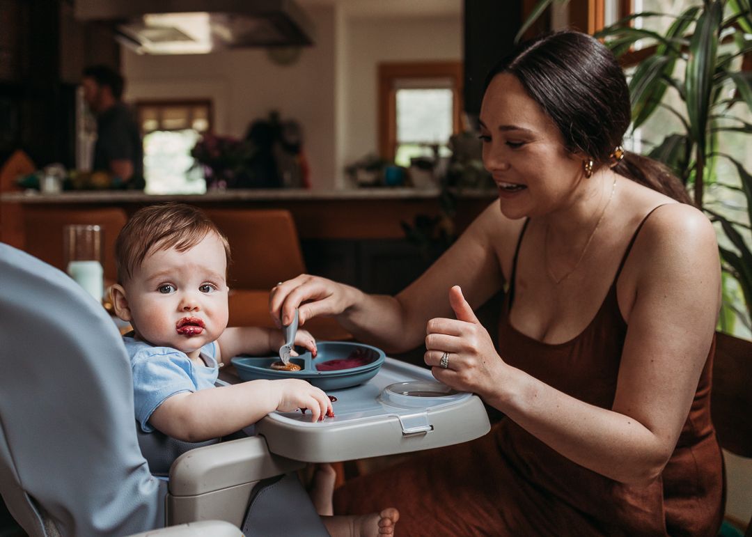 Parent and baby seated at dining table with toddler positioned in a blue highchair during mealtime.