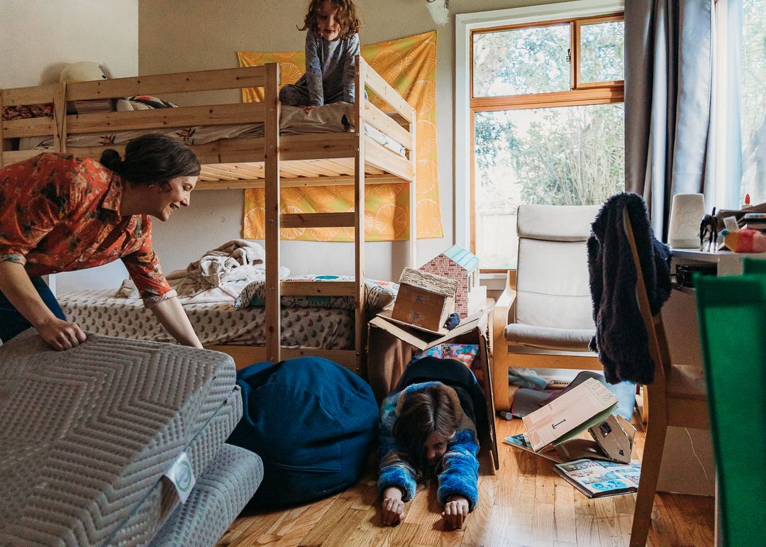 Students relax and study in a dorm room with wooden bunk beds, textbooks, and natural lighting through windows.