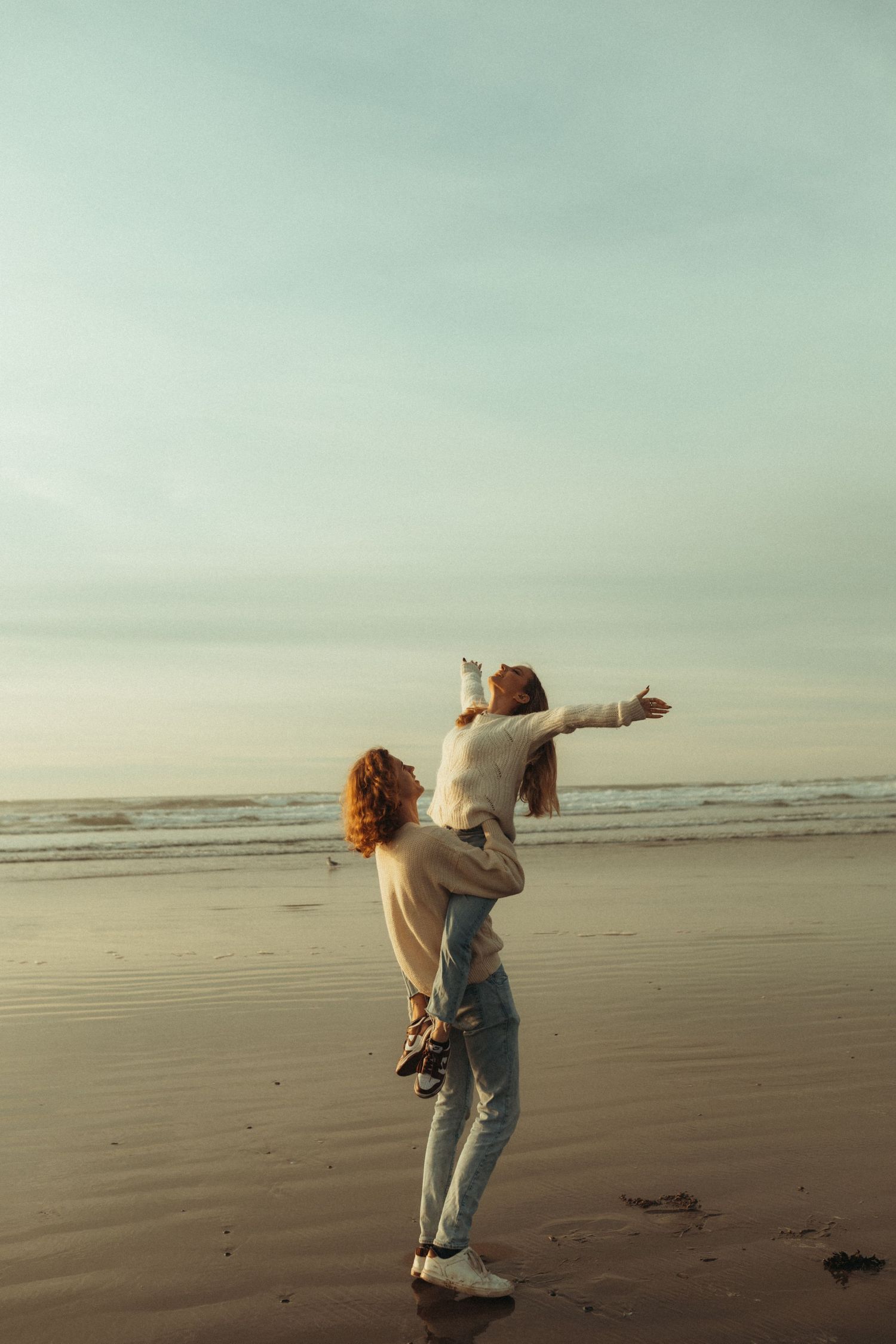 A couple sits together on coastal rocks at sunset watching the glistening ocean waves below.