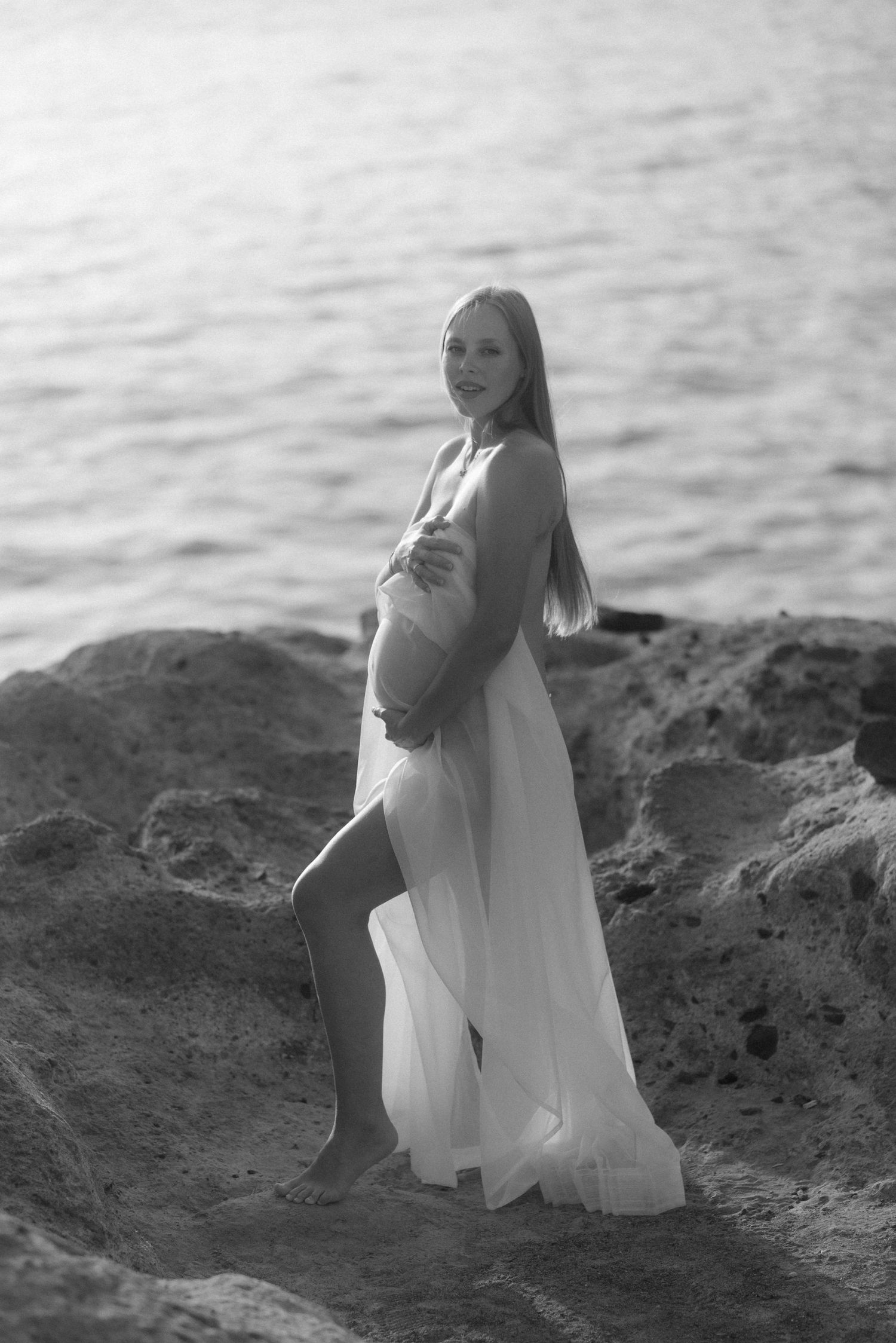 A series of artistic black and white photographs showing someone in a white dress posing on rocky coastal terrain.