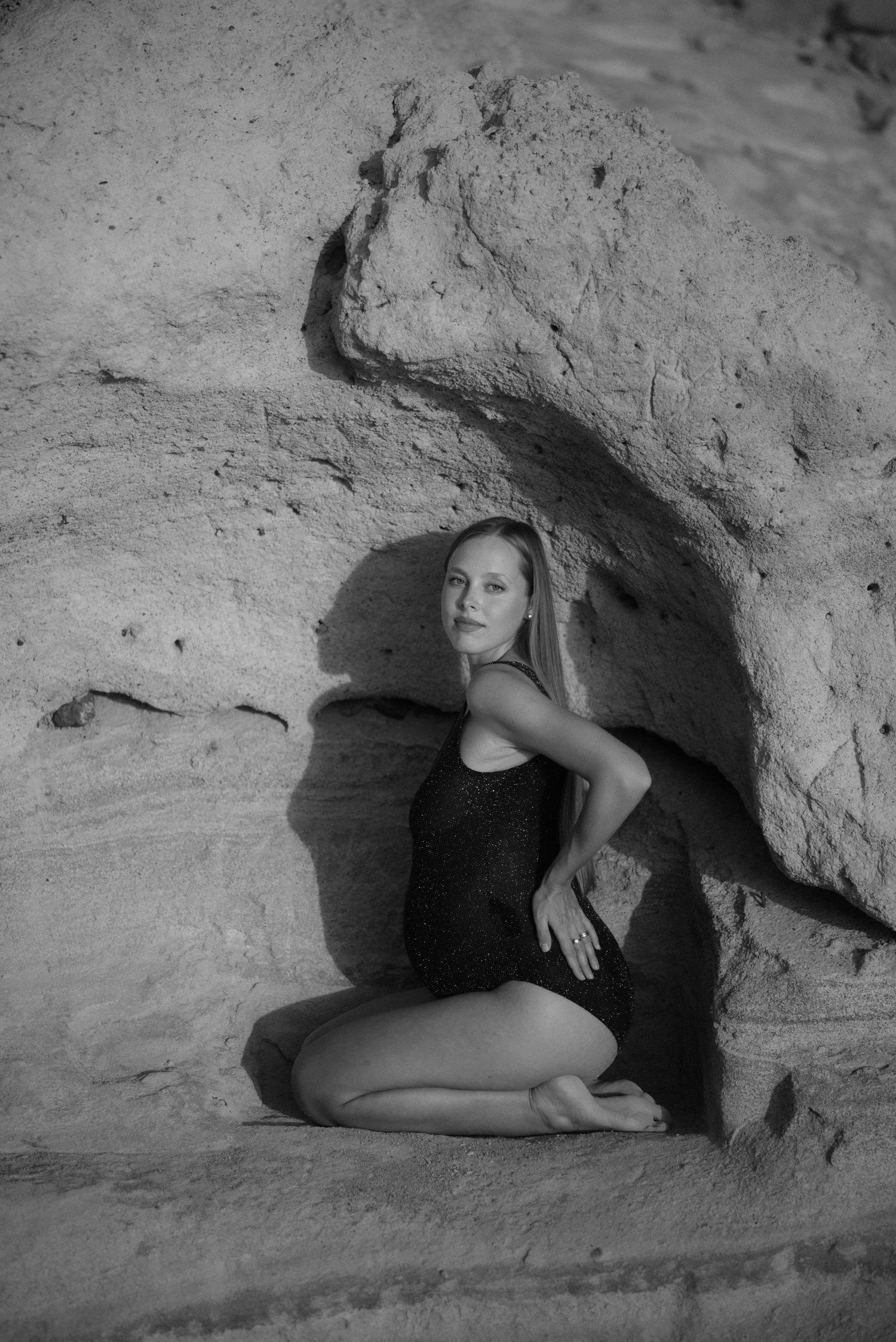 Black and white portrait of woman in bodysuit sitting in natural rock cave formation.