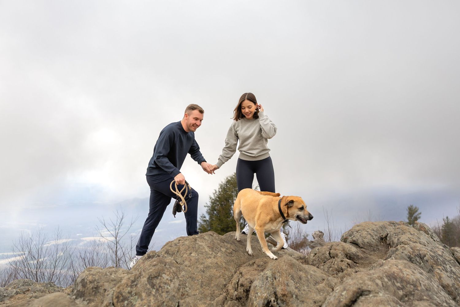 A group enjoys hiking with their golden retriever on a rocky trail overlooking a scenic landscape view.