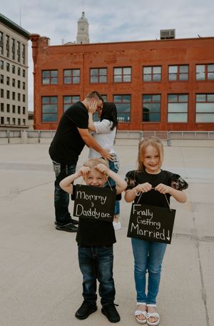 Three children holding chalkboard signs on a rooftop announcing their parents' marriage.