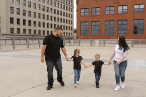 Family members walking in a line on a rooftop plaza with brick buildings behind them.