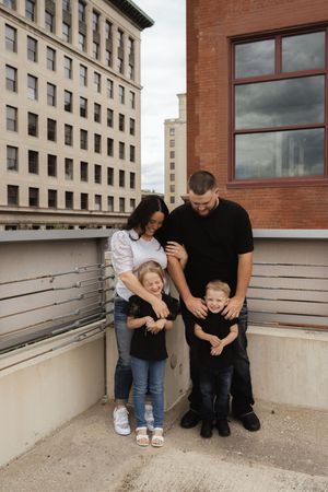 A playful family moment captured against an urban backdrop with brick buildings and concrete walls.
