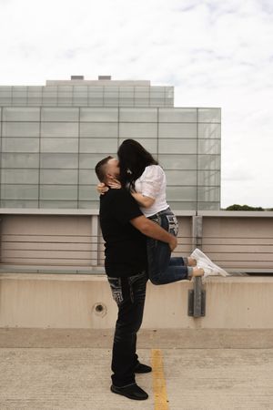 Couple embracing and lifting in celebration on a rooftop parking structure.