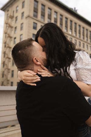 A romantic couple kissing against a backdrop of historic architecture.