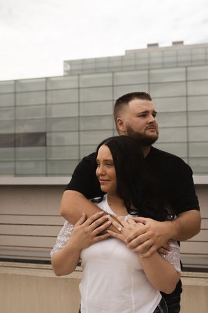 Happy couple in black and white outfits embracing on a rooftop with modern buildings in background.