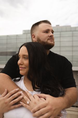 Couple sharing an intimate moment while showing off an engagement ring on a rooftop.