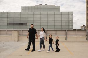 Wide shot of couple on empty rooftop parking area with city buildings visible.