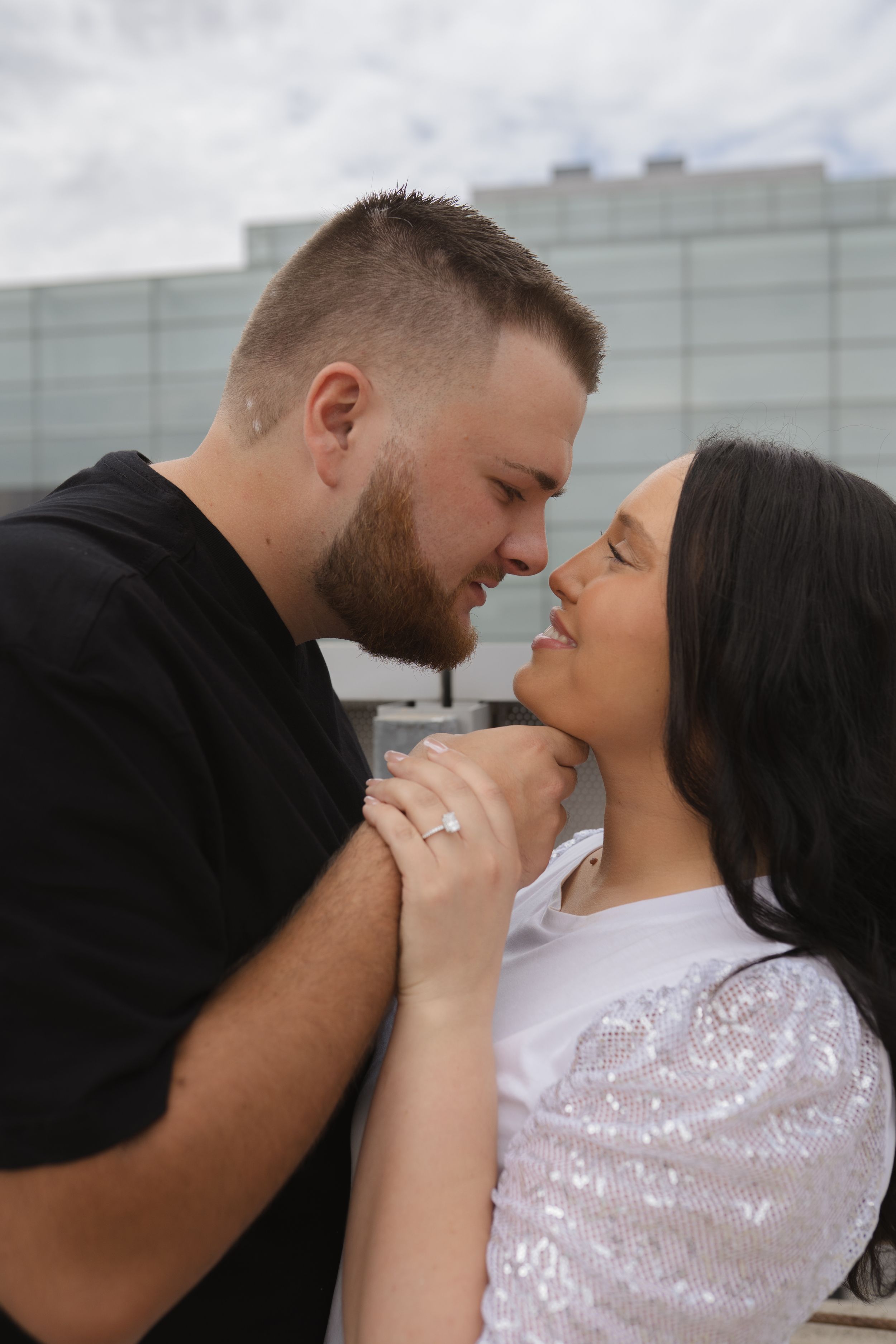 Intimate couple sharing tender moments against an industrial white building backdrop.