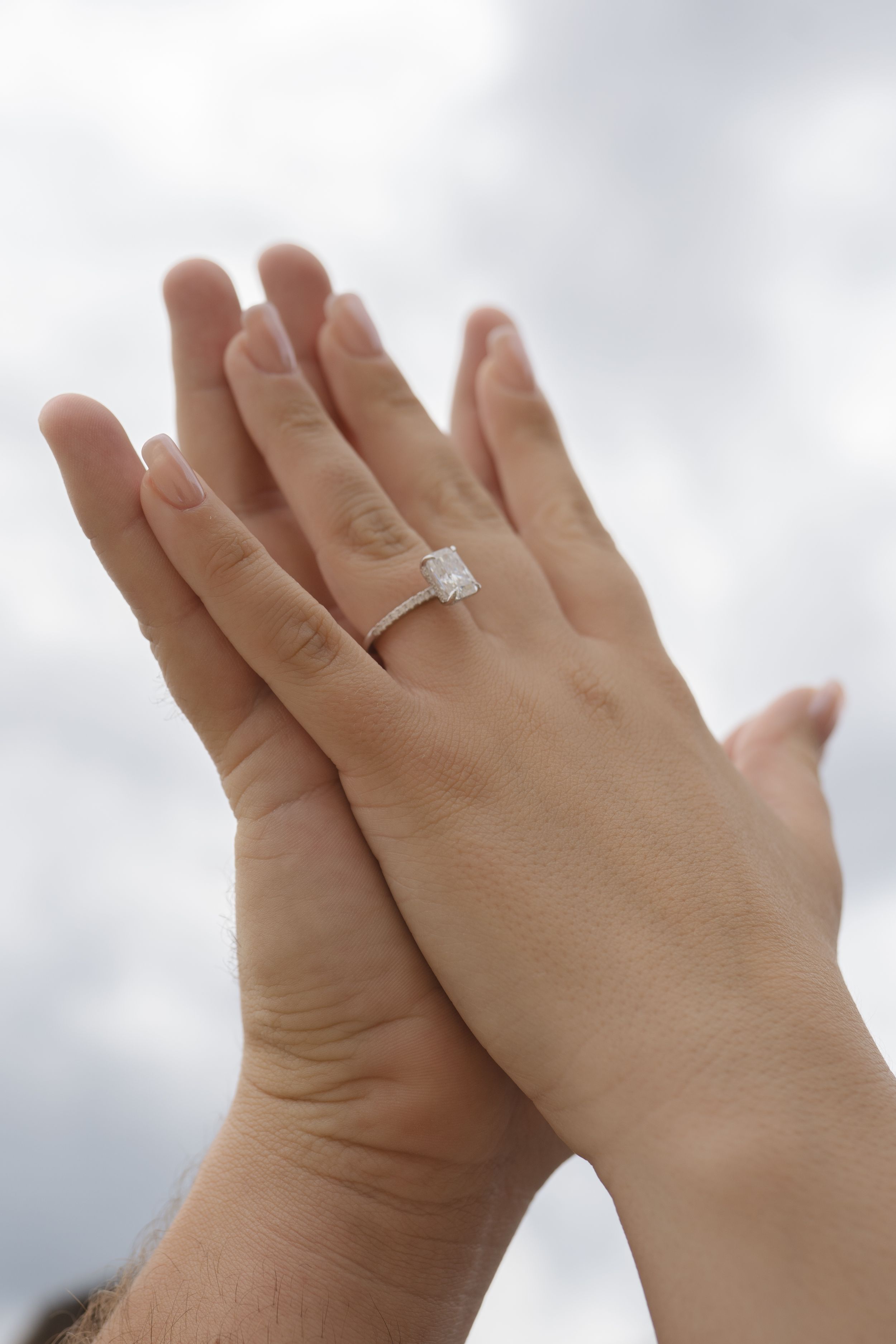 Close-up of hands with an engagement ring against a cloudy sky background.