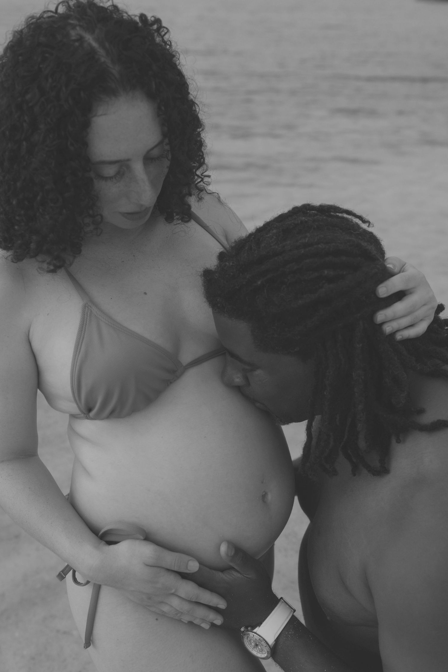 Intimate maternity beach portrait in black and white showing tenderness and connection.