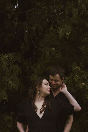 A couple in dark clothing sharing a tender moment against evergreen trees.