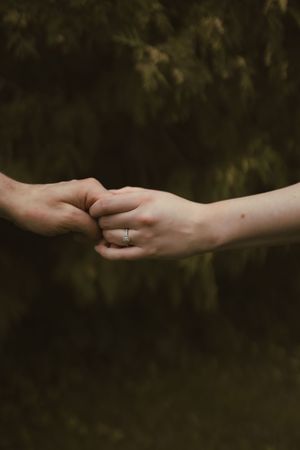 Two hands gently reaching towards each other against a dark natural background.