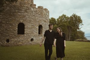 A couple walks hand in hand near a historic stone tower structure.