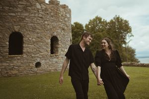 Two people in black outfits share an intimate moment by ancient stone ruins.