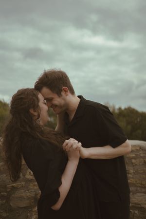 A couple dressed in black embraces tenderly on a cloudy afternoon.